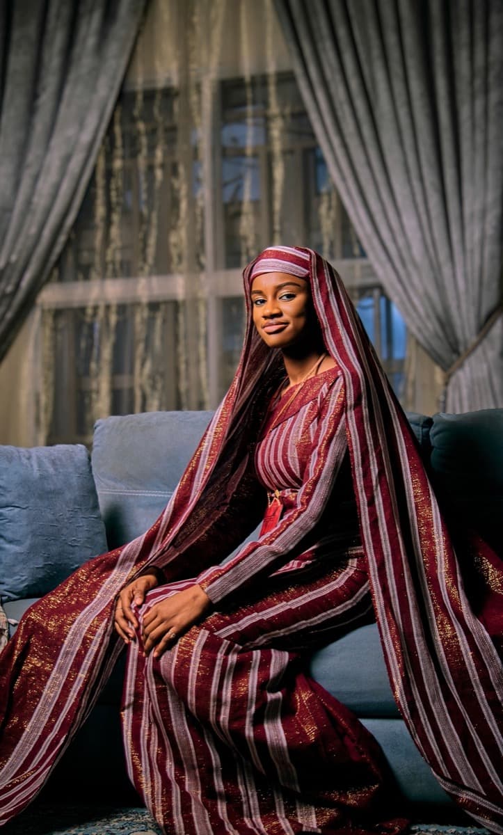 A woman wrapped in a maroon and cream striped aso oke shawl with fringe and metallic thread detailing
